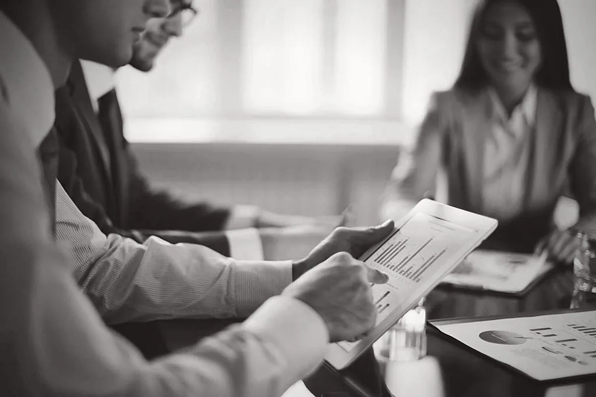 Two people reviewing printed reports across a desk, photographed in black and white